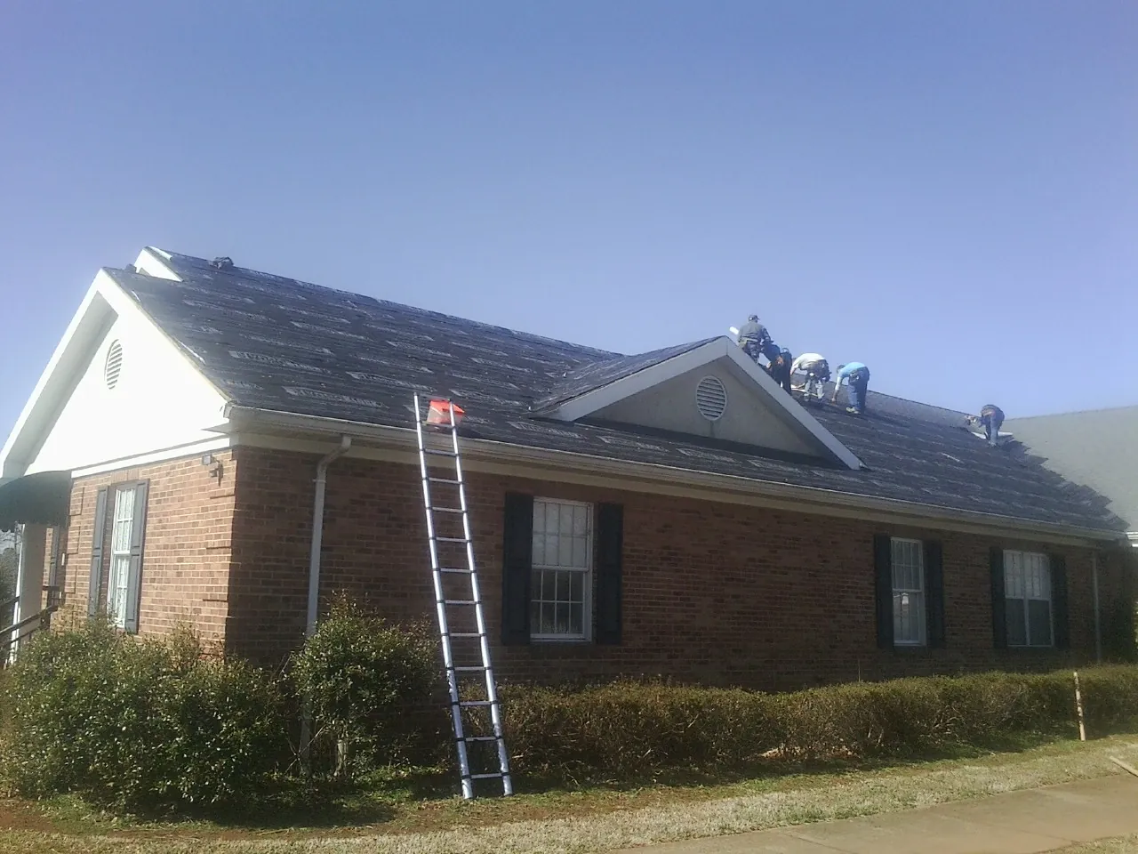 Crew tearing shingles off a brick ranch roof with a ladder set — Metal Roof Repair work by our crew in Maine
