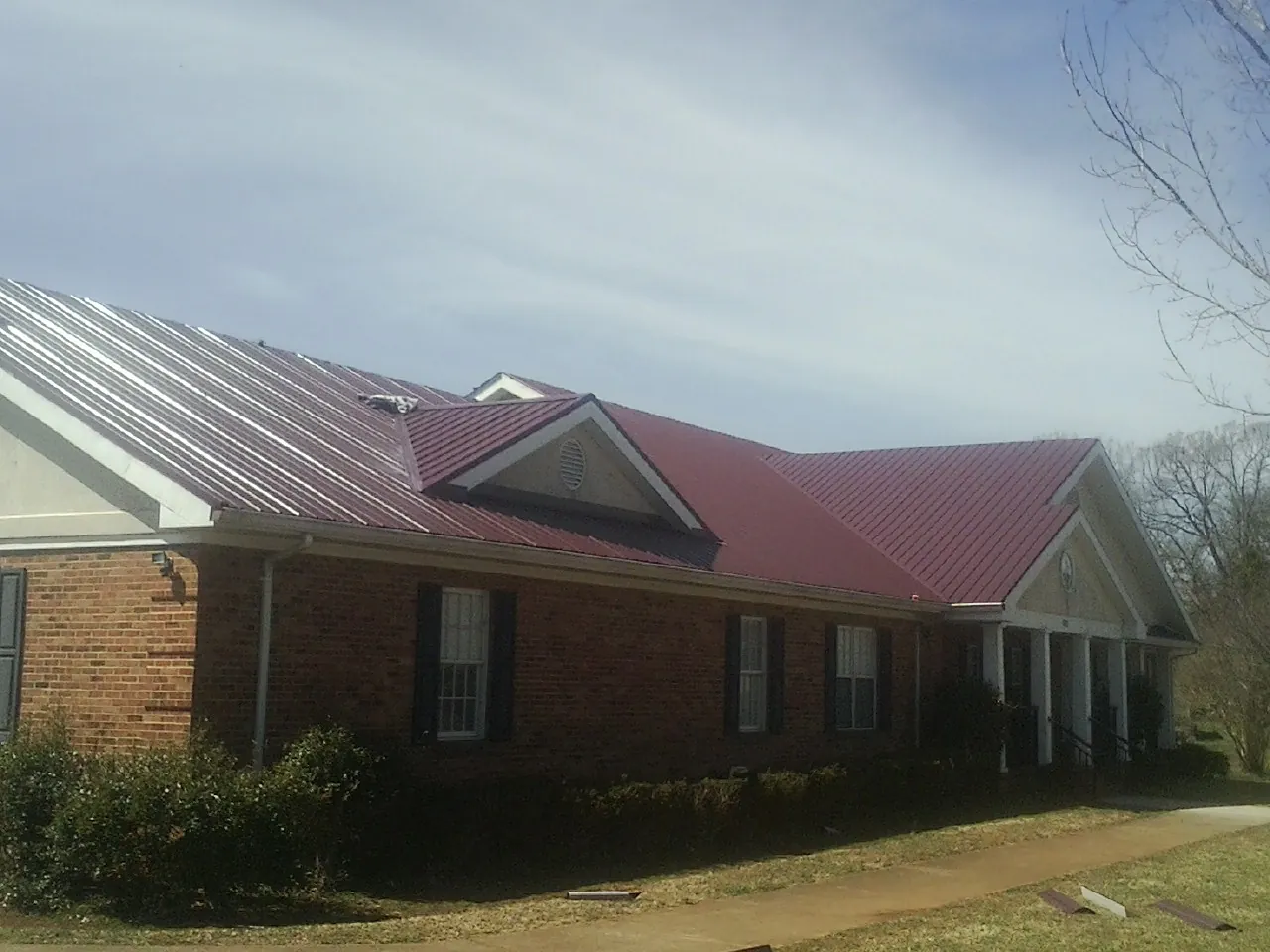 Red metal roof with gabled entries on a long brick building, from a Hail Damage Roof Repair job in Maine