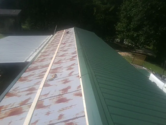 Old rusted panels beside newly installed green metal roofing — Wind Damage Roof Repair by Roofing Brothers in Maine