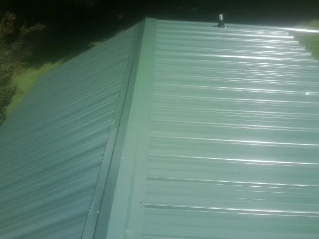 New green metal panels meeting at the ridge of a roof — Flat Roof Repair work by our crew in Maine