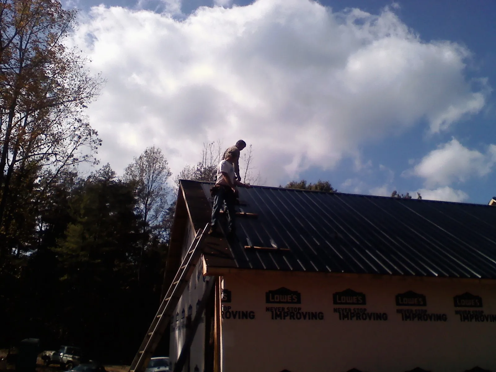 Roofer fastening dark metal panels high against a cloudy sky, from a Roof Inspection job in Maine