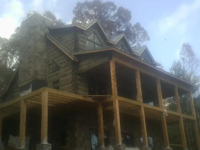 Stone chimney and dormers on a large log home with a timber porch in Maine