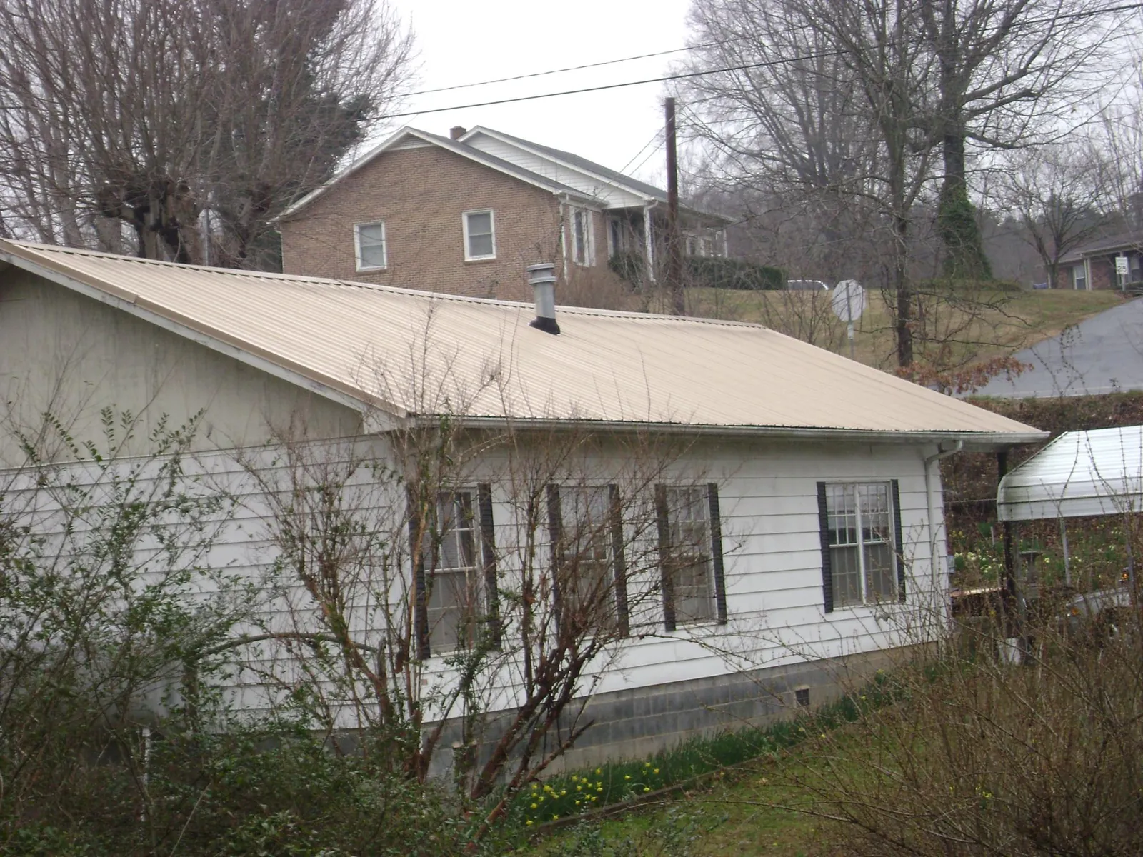 Tan metal roof on a white sided house set into a hillside — Commercial Roofing by Roofing Brothers in Maine