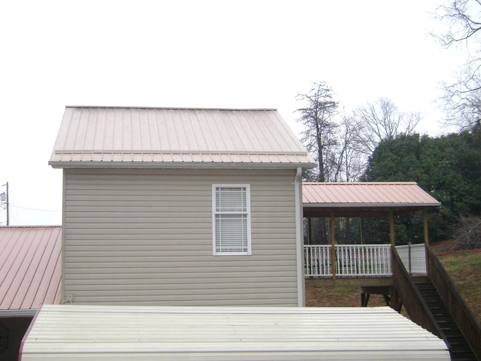 Tan metal roofs on a two story addition and attached porch, from a Roof Replacement job in Maine