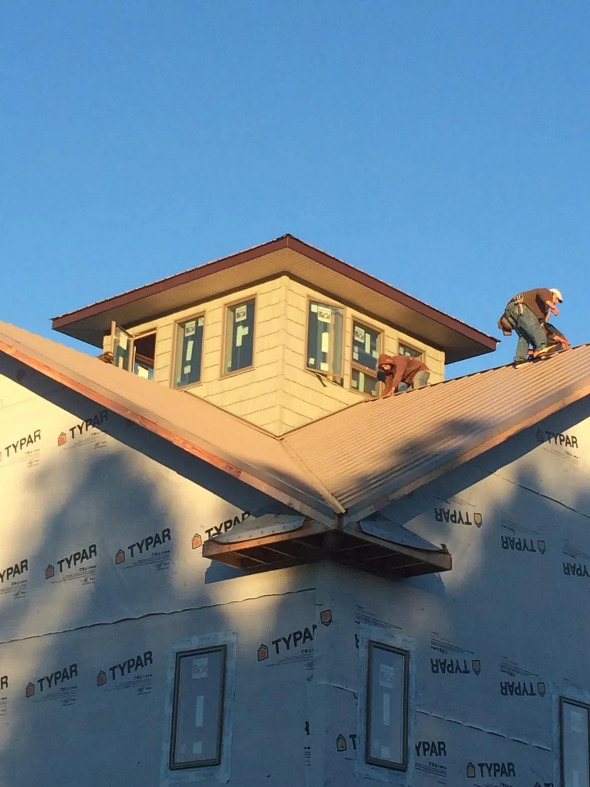 Roofers working around a rooftop cupola on a new metal roof at sunset — Roof Waterproofing in Maine by Roofing Brothers